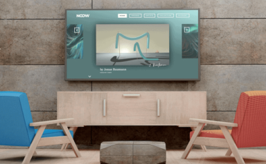 TV an der Wand mit NOOW auf dem Bildschirm, davor eine Sitzgruppe mit einem Holztisch sowie einem roten und einem blauen Stuhl