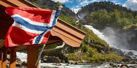 Norwegische Flagge an Hausdach mit Wasserfall und Bergen im Hintergrund