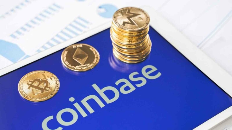 Coinbase Logo auf Tablet mit physischen Krypto-Coins