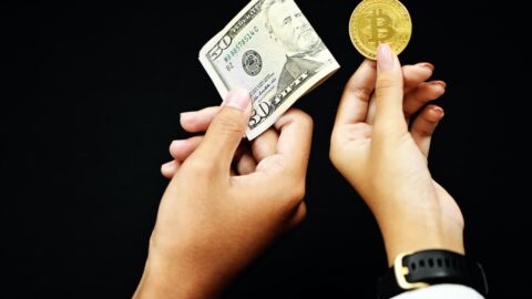 Zwei Hände halten einen Dollarschein und einen Bitcoin
