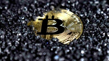 goldene Bitcoin Münze versinkt in schwarzer Kohle