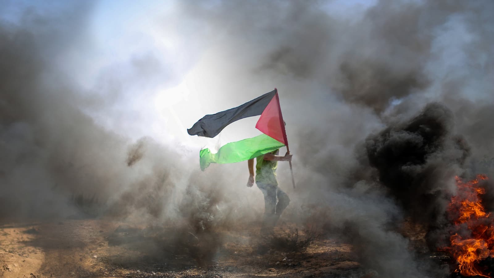 Mann trägt eine Flagge Palästinas in der Nähe eines Feuers