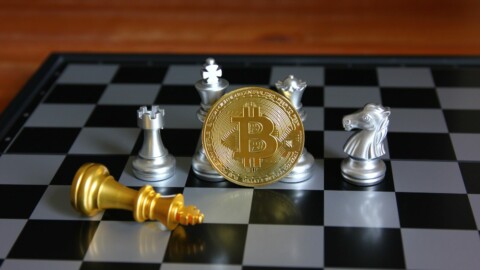 BTC Coin vor silbernen Schachfiguren auch Schachbrett