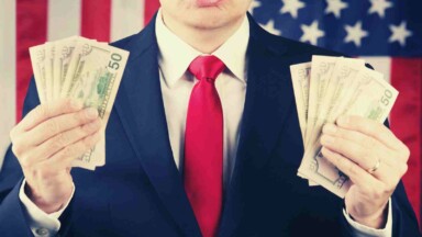 Mann im Anzug hält Dollarnoten vor USA Flagge