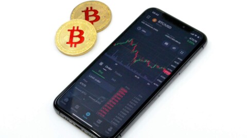 zwei bitcoin m&uuml;nzen neben einem smartphone auf weissem grund