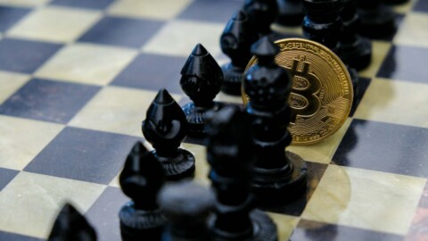 bitcoin münze auf schachbrett zwischen schachfiguren