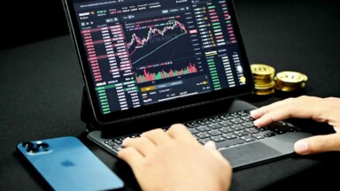 trader am laptop mit trading chart, smartphone und geldmünzen