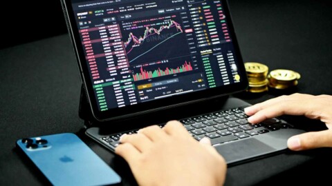 trader am laptop mit trading chart, smartphone und geldm&uuml;nzen
