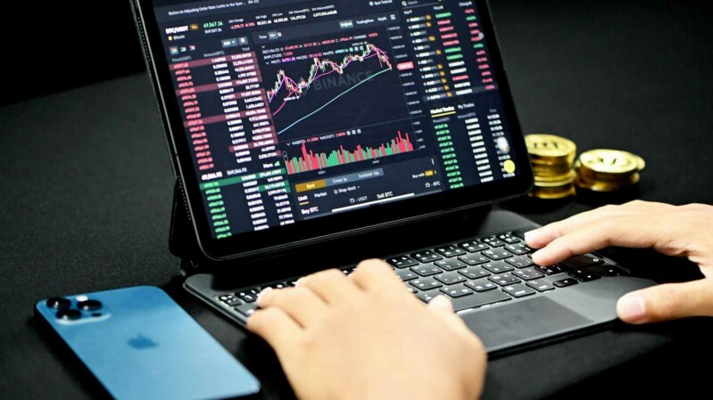 trader am laptop mit trading chart, smartphone und geldmünzen