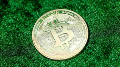 eine physische bitcoin münze vor einem grünen hintergrund