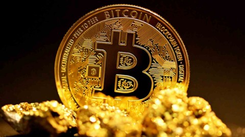 goldklumpen liegen vor einer stehenden bitcoin münze