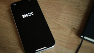 okx logo auf einem smartphone welches auf einem tisch liegt